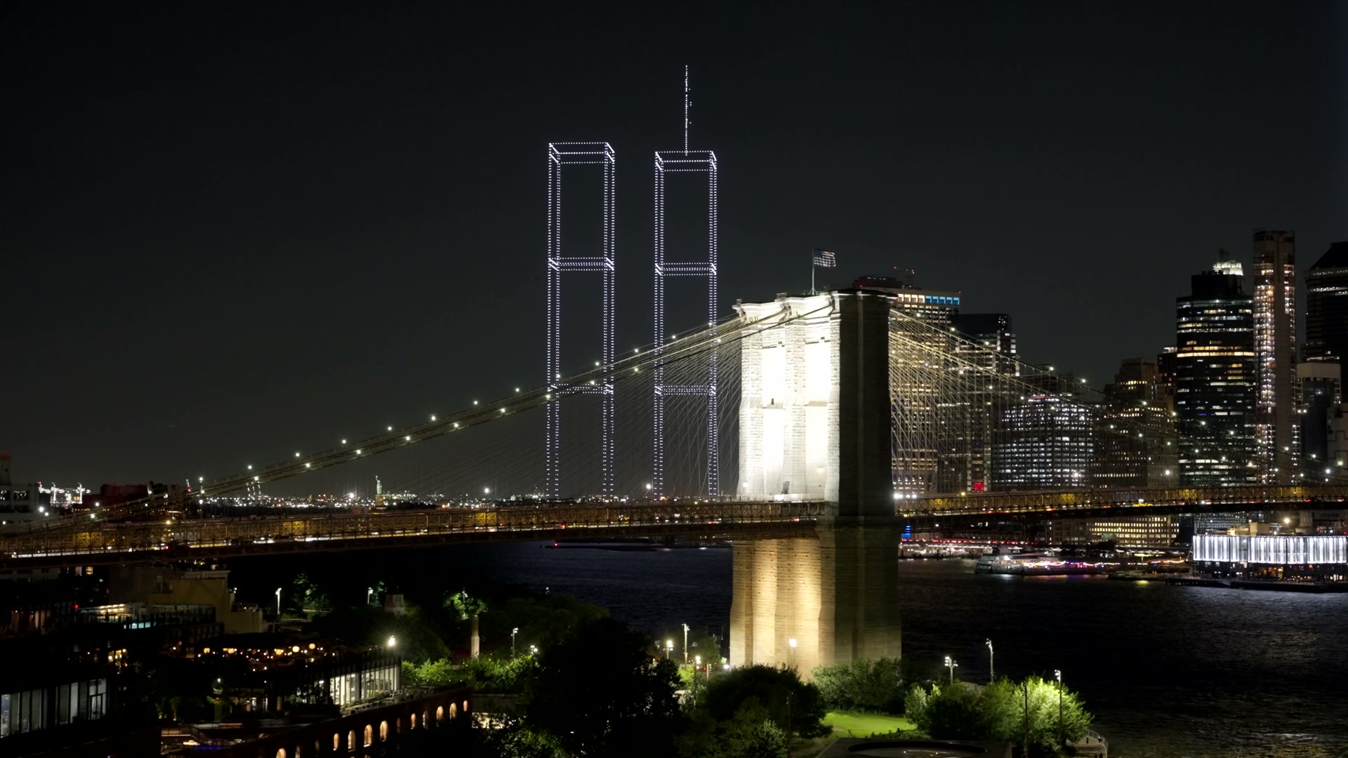 Film of the lit Brooklyn Bridge at night with two towers of light standing behind it