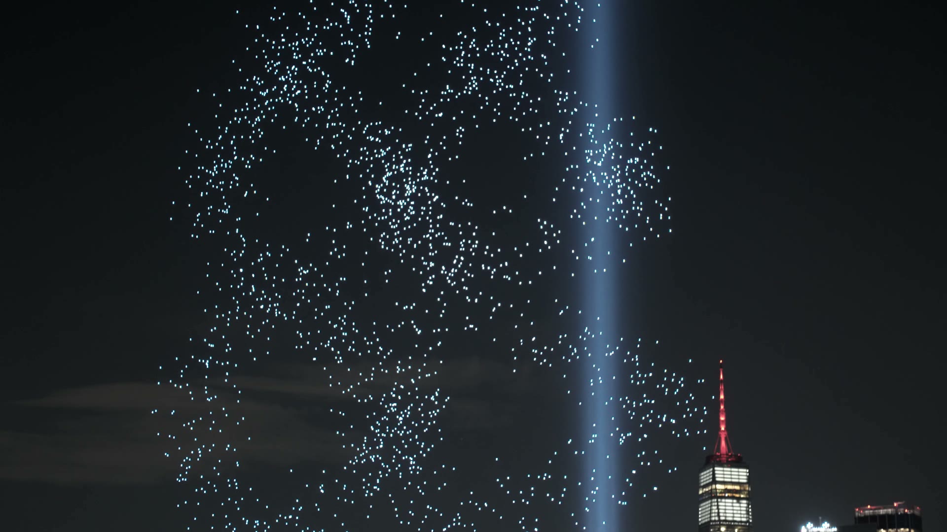 Film of thousands of lights turning in a helix in the night sky beside the Tribute in Light
