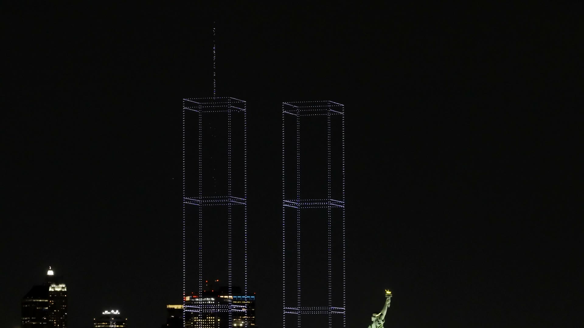 Film of two towers of light over New York Harbor with the Statue of Liberty lit at right