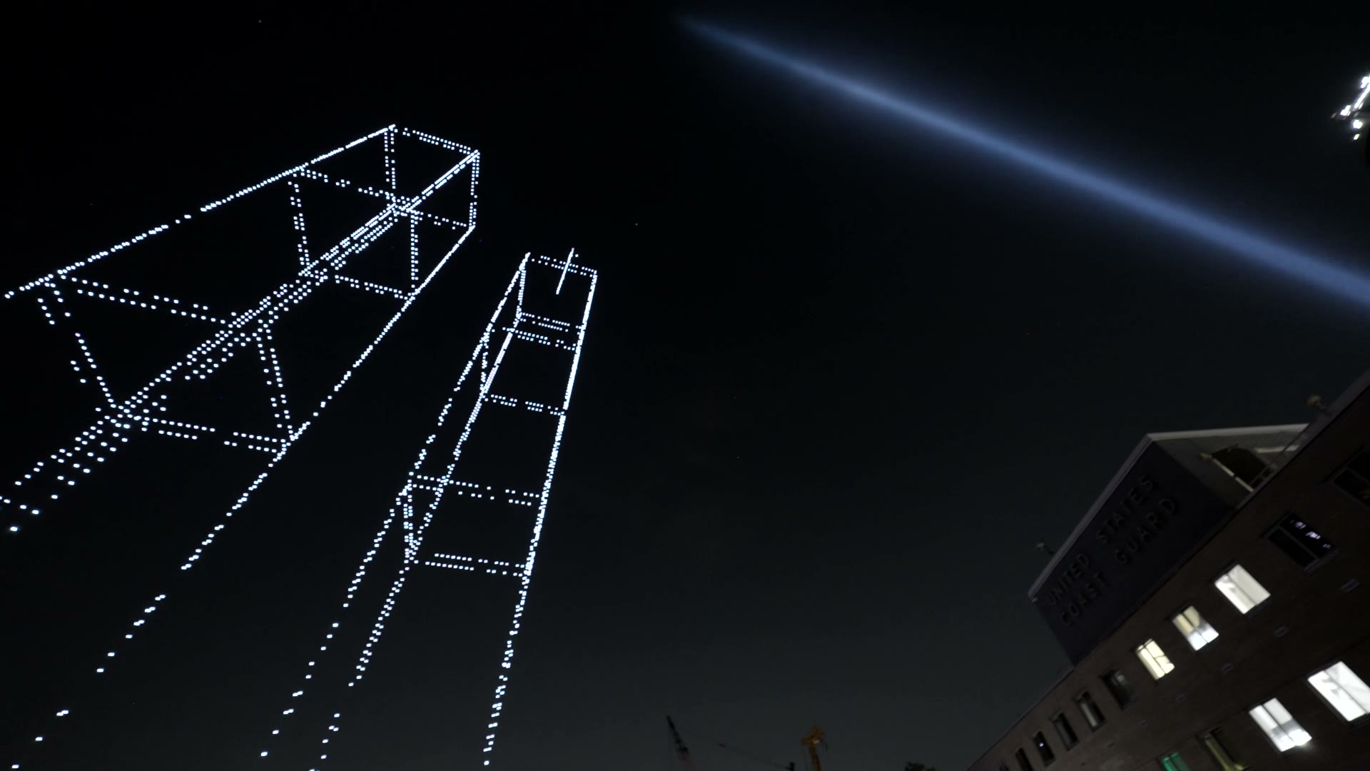 Film looking up as lines of lights climb into the night sky above buildings